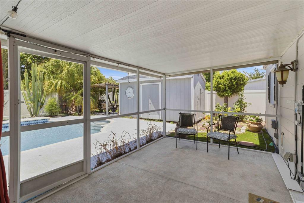 A screened-in patio with a concrete floor overlooks a swimming pool and a storage shed — 2713 W BRADDOCK STREET, TAMPA, FL