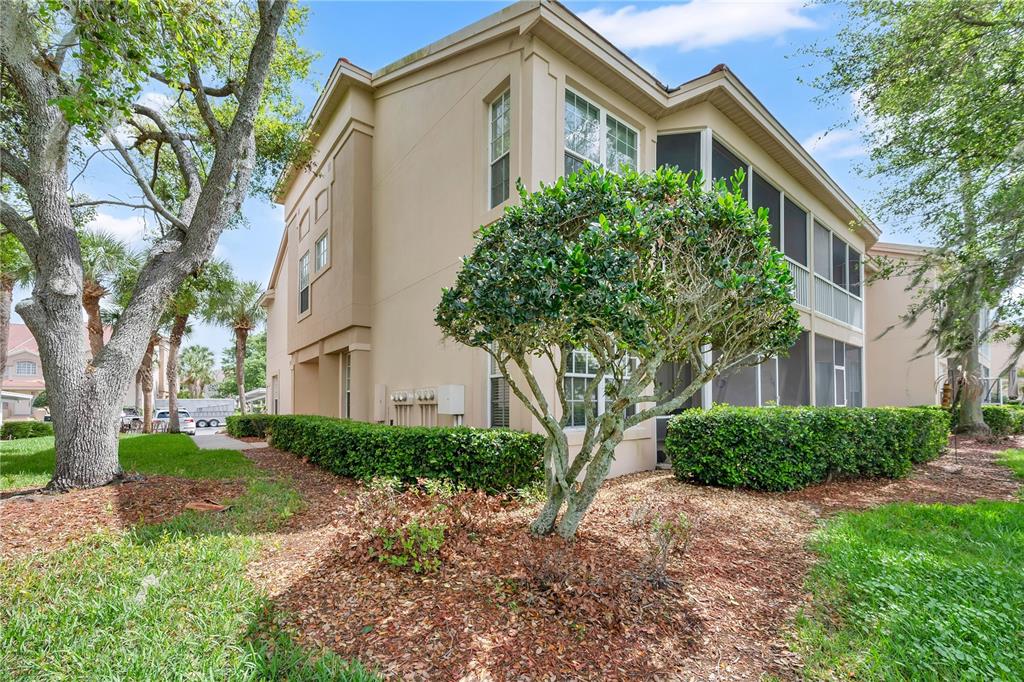 A beige two-story building with a screened-in porch, surrounded by landscaping and mature trees — 427 ENCLAVE PLACE UNIT 427, LAKELAND, FL