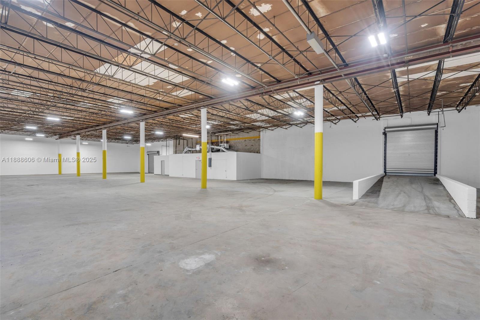 An empty industrial warehouse space features concrete floors, yellow-painted support columns, and a loading ramp — 333 W 75th Pl # 1D, Hialeah FL 33014, HIALEAH, FL