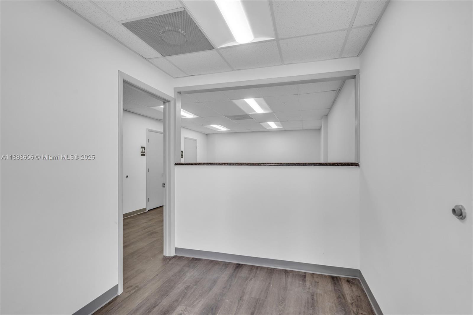 An office interior features a pass-through window, white walls, and wood-look flooring — 333 W 75th Pl # 1D, Hialeah FL 33014, HIALEAH, FL