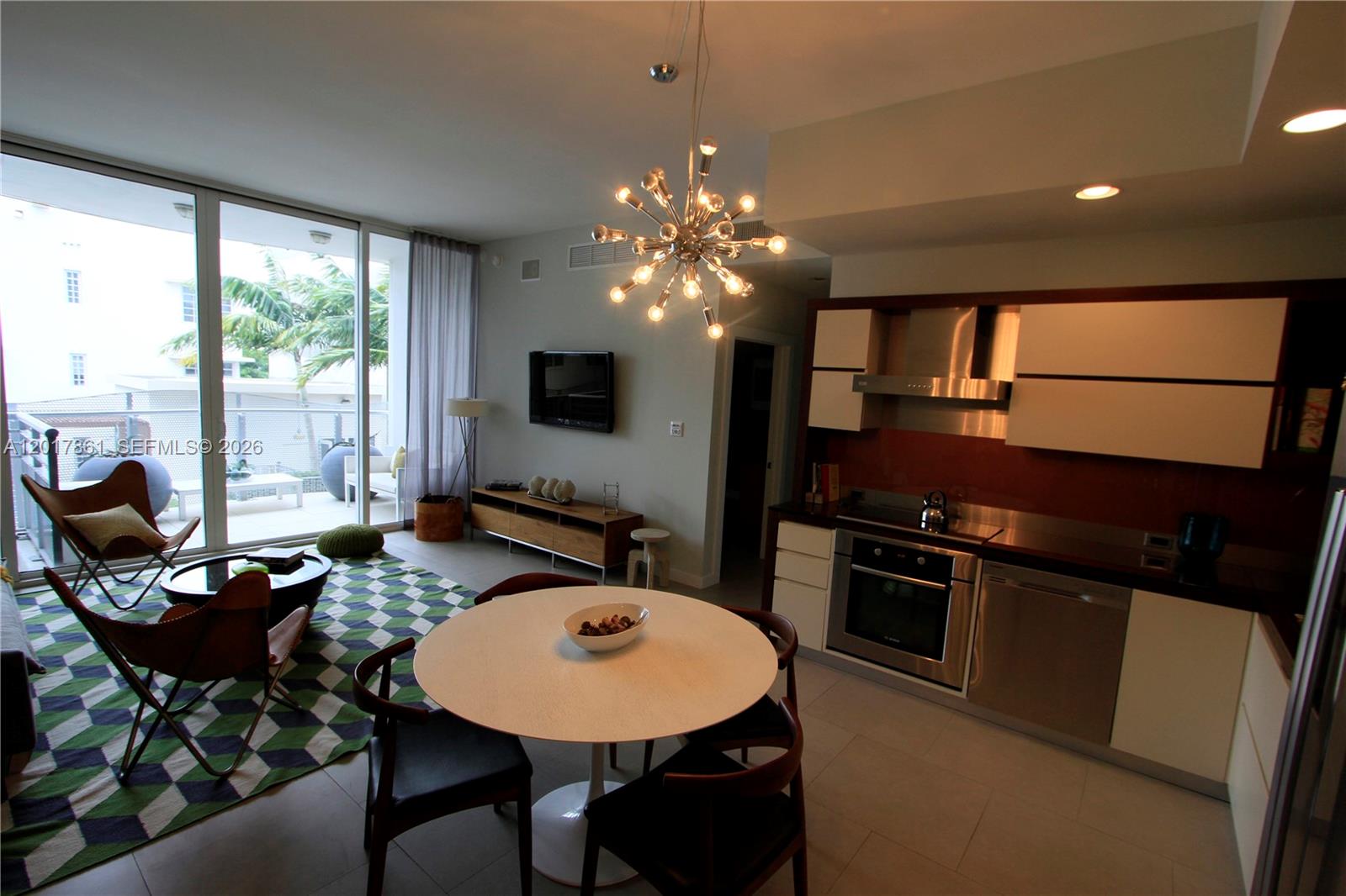 A modern open-concept living and dining area features a kitchen, balcony, and geometric rug — 2100 Park Ave # 202, Miami Beach FL 33139, MIAMI BEACH, FL