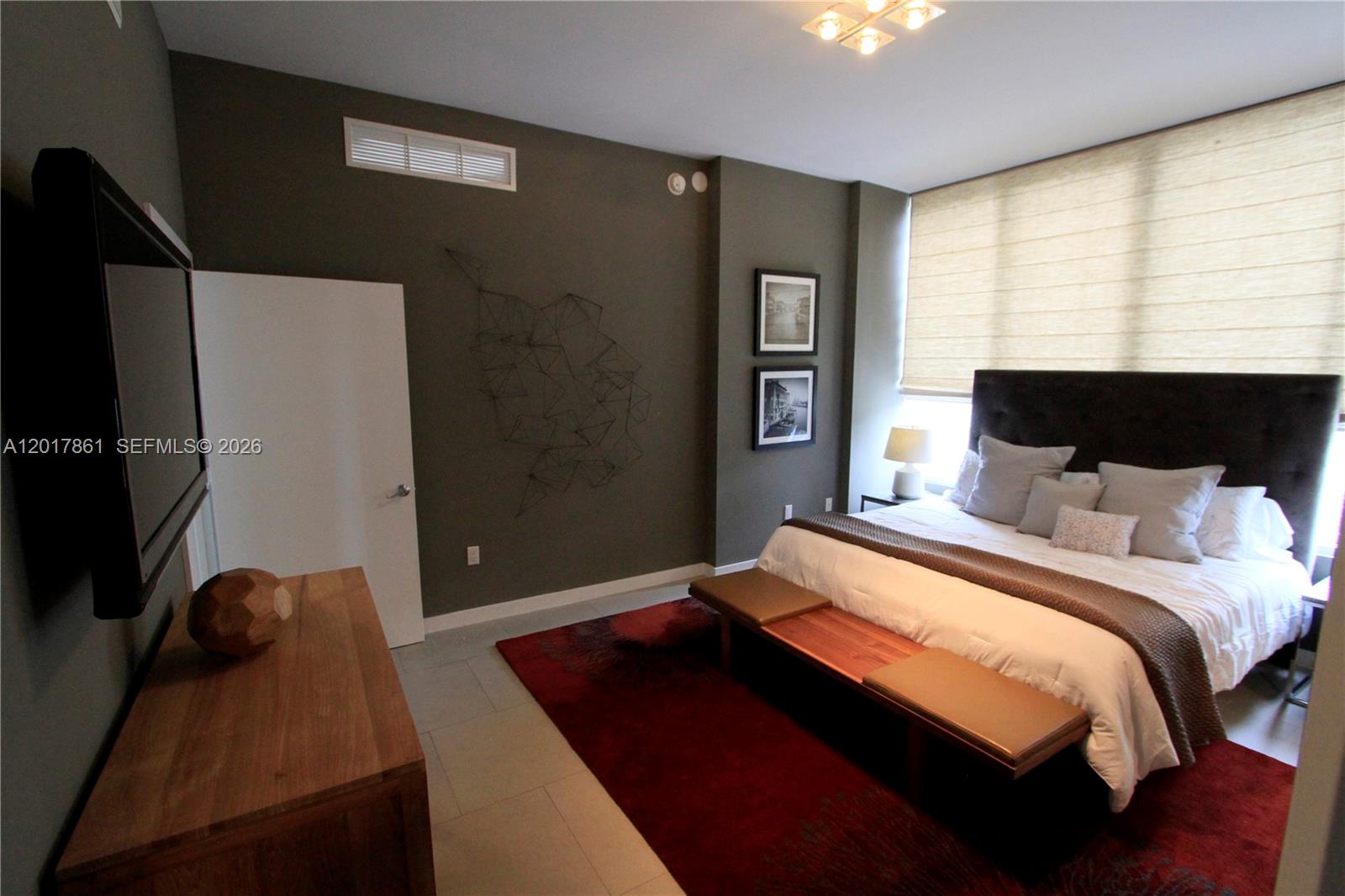 A bedroom features a bed, a wooden bench, a red rug, and a wall-mounted television — 2100 Park Ave # 202, Miami Beach FL 33139, MIAMI BEACH, FL