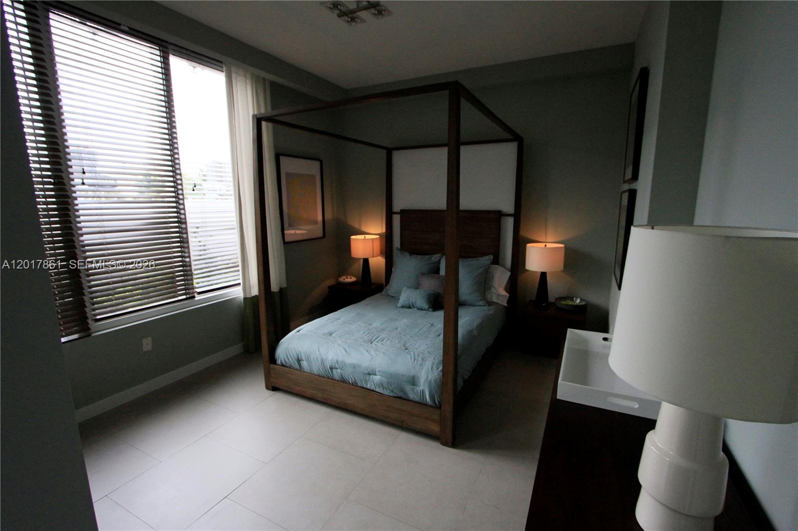 A bedroom features a wooden canopy bed, light blue bedding, and large windows with blinds — 2100 Park Ave # 202, Miami Beach FL 33139, MIAMI BEACH, FL