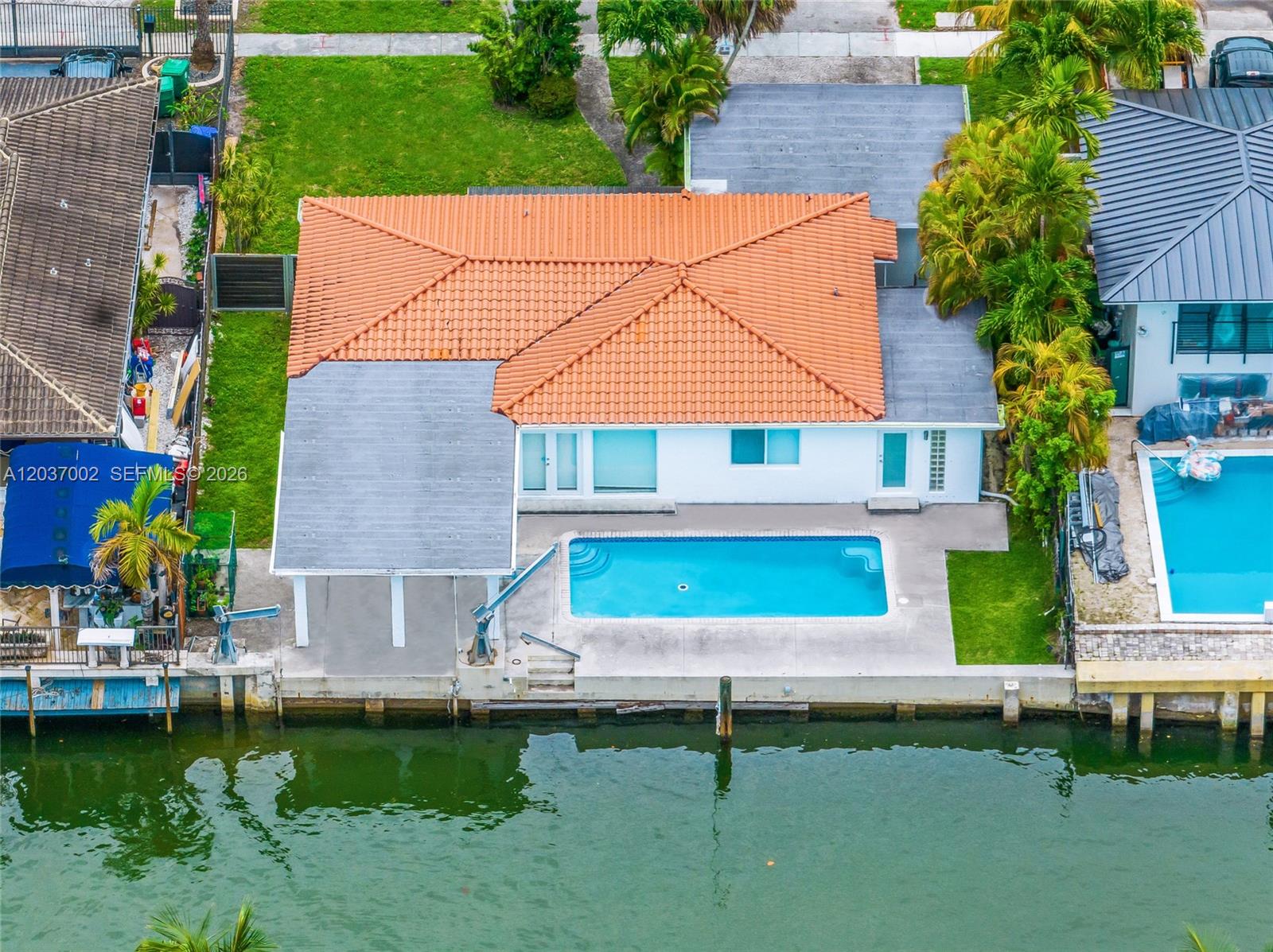 An aerial view shows a waterfront house with a tiled roof, pool, and boat lift — 1161 NE 86th St, Miami FL 33138, MIAMI, FL