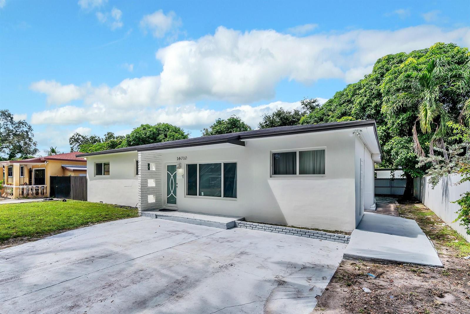 A single-story white house with a concrete driveway and a flat roof under a blue sky — 16010 NE 5th Avenue, Miami FL 33162, MIAMI, FL