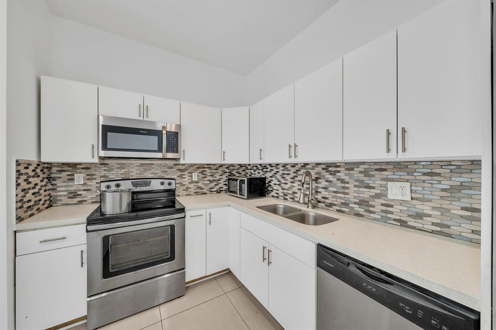 A kitchen featuring white cabinets, stainless steel appliances, a tiled backsplash, and light-colored countertops — 16010 NE 5th Avenue, Miami FL 33162, MIAMI, FL