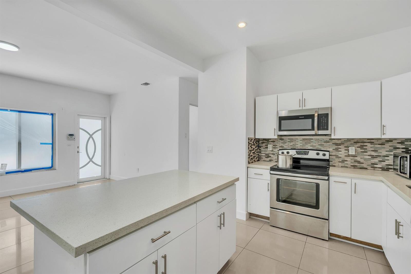 A modern kitchen features white cabinets, stainless steel appliances, a quartz island, and tile flooring — 16010 NE 5th Avenue, Miami FL 33162, MIAMI, FL