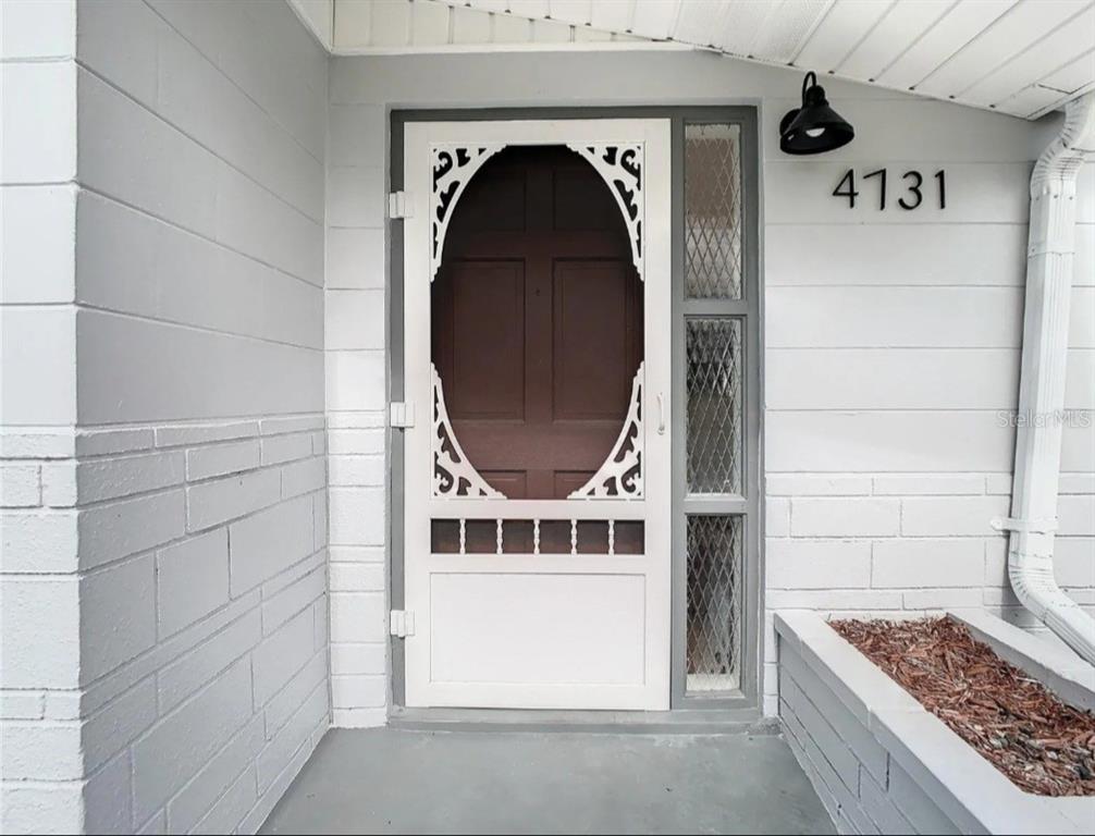 A white front door with a decorative screen and a side window on a porch — 4731 PHOENIX AVENUE, HOLIDAY, FL
