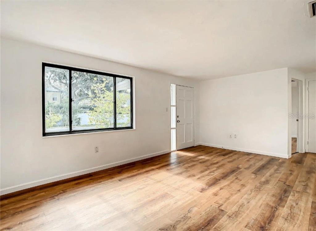 An empty living room features white walls, wood-look flooring, and a large window — 4731 PHOENIX AVENUE, HOLIDAY, FL