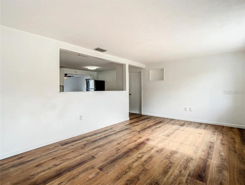 An empty room with wood-look flooring and a pass-through window looking into a kitchen — 4731 PHOENIX AVENUE, HOLIDAY, FL