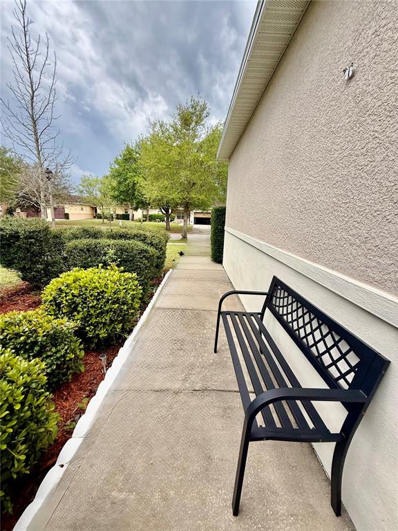 A black metal bench sits on a concrete walkway beside a beige stucco exterior wall — 4029 MARINA ISLE DRIVE, KISSIMMEE, FL