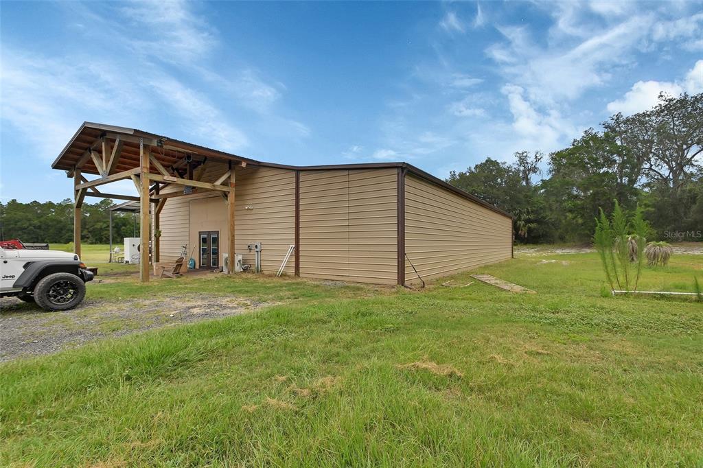 A tan metal building with a covered porch stands in a grassy field — 4940 STATE ROAD 11, DE LEON SPRINGS, FL