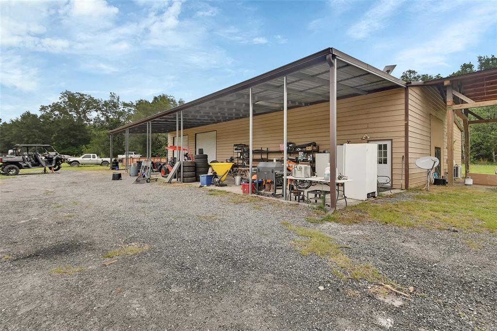 A gravel lot leads to a metal-sided workshop building with an attached open-air carport — 4940 STATE ROAD 11, DE LEON SPRINGS, FL