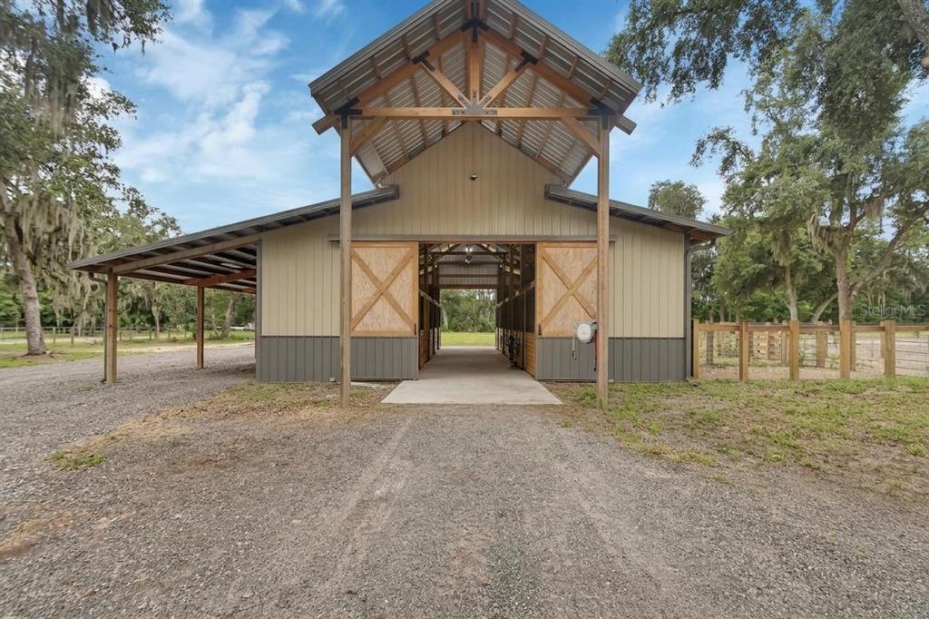 A wooden barn with a metal roof and open center aisle stands on a gravel lot — 4940 STATE ROAD 11, DE LEON SPRINGS, FL