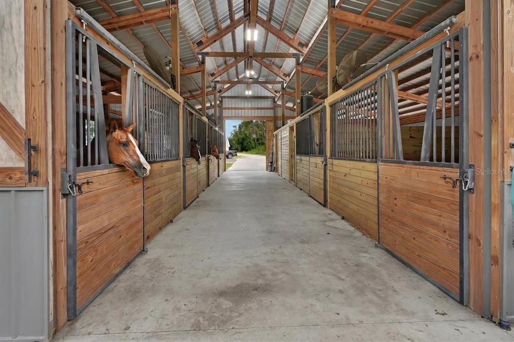 A horse stable aisle features concrete flooring and wooden stalls with metal bars — 4940 STATE ROAD 11, DE LEON SPRINGS, FL