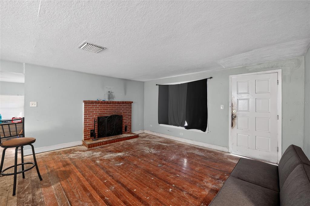A living room features a brick fireplace, hardwood floors, a white door, and a window — 10109 MAIN STREET, THONOTOSASSA, FL