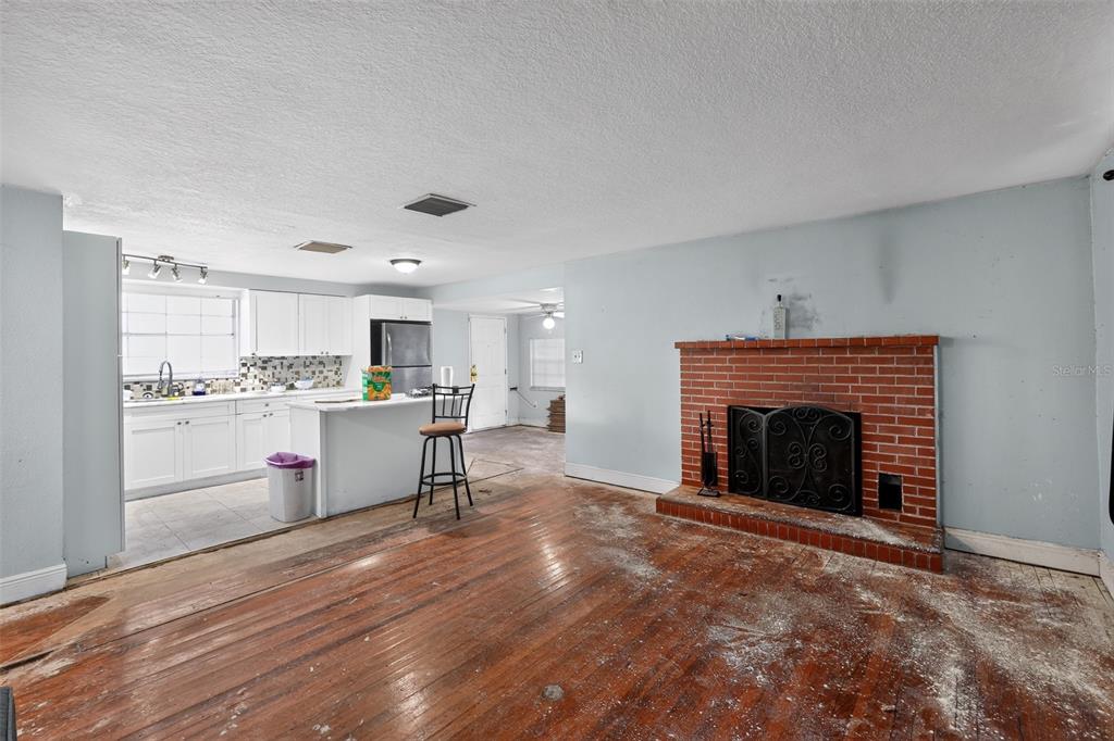 A living room with a brick fireplace and hardwood floors opens into a white kitchen — 10109 MAIN STREET, THONOTOSASSA, FL