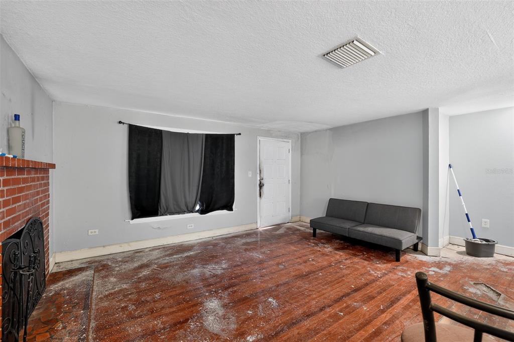 An empty living room features hardwood floors, a brick fireplace, and a gray sofa — 10109 MAIN STREET, THONOTOSASSA, FL