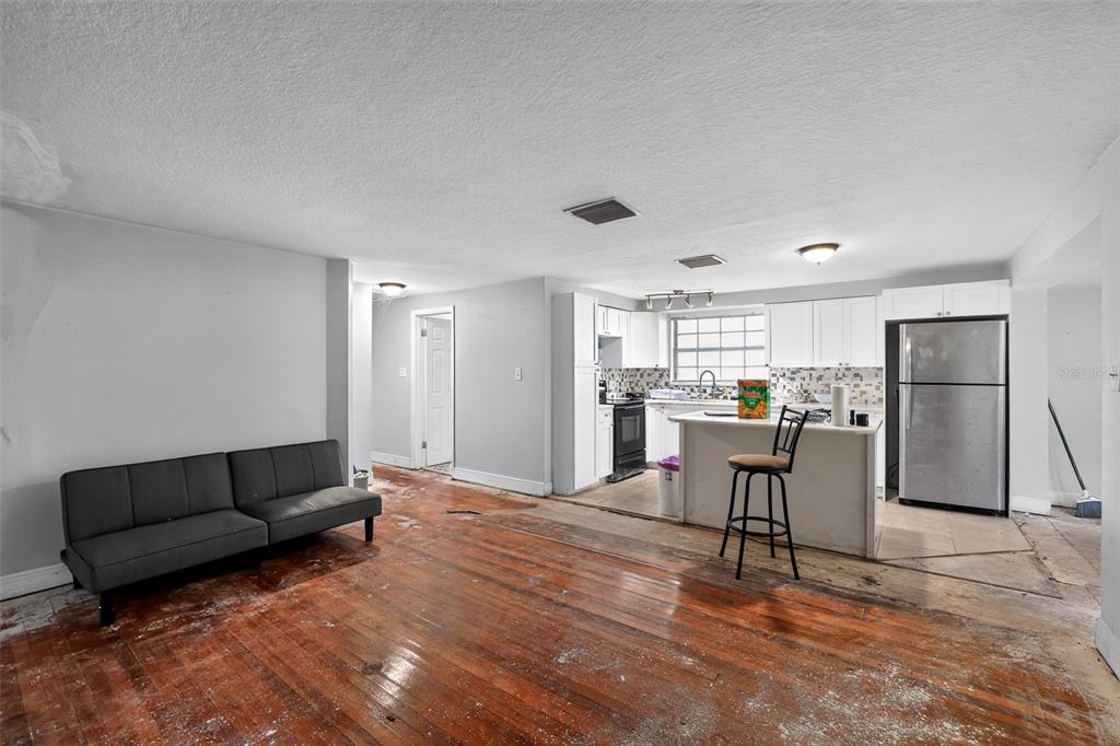 A living room with hardwood floors and a sofa leads into an open kitchen area — 10109 MAIN STREET, THONOTOSASSA, FL
