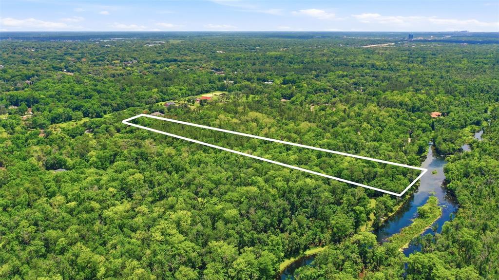 An aerial view shows a rectangular plot of land outlined in white amidst dense forest — DELK ROAD, LONGWOOD, FL