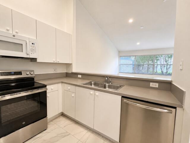 A kitchen features white cabinets, stainless steel appliances, a double sink, and light-colored flooring — 2480 S Coral Trace Circle S, Delray Beach FL 33445, DELRAY BEACH, FL
