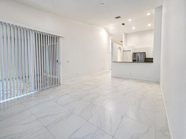 An open-concept living area features white marble-look tile flooring and a kitchen with stainless appliances — 2480 S Coral Trace Circle S, Delray Beach FL 33445, DELRAY BEACH, FL