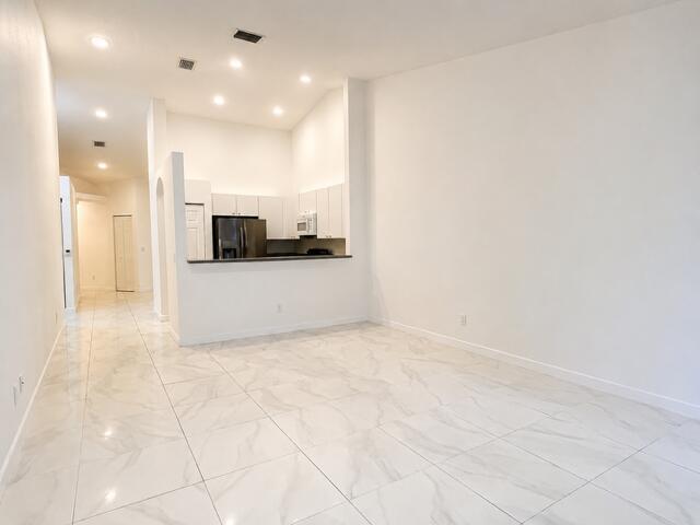 An open-concept living area features white marble-look tile flooring and a kitchen with white cabinets — 2480 S Coral Trace Circle S, Delray Beach FL 33445, DELRAY BEACH, FL