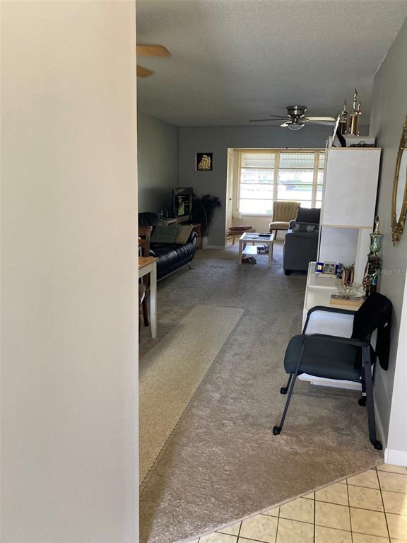 A living room features carpeted flooring, a ceiling fan, and a view toward a window — 5660 80TH STREET N UNIT B107, ST PETERSBURG, FL