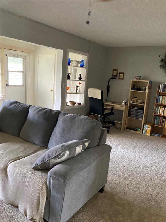 A living room features a grey sofa, a built-in display niche, and a home office area — 5660 80TH STREET N UNIT B107, ST PETERSBURG, FL