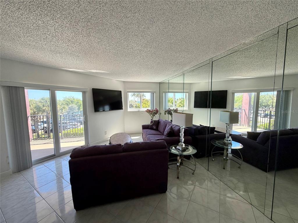 A living room features purple sofas, tiled floors, a mirrored wall, and a sliding glass door — 180 SE 20TH AVENUE UNIT 303, DEERFIELD BEACH, FL