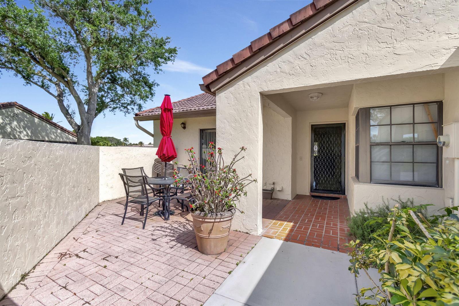 A patio with a brick floor, outdoor dining set, and a front entrance with a door — 5531 Parkwalk Circle E, Boynton Beach FL 33472, BOYNTON BEACH, FL