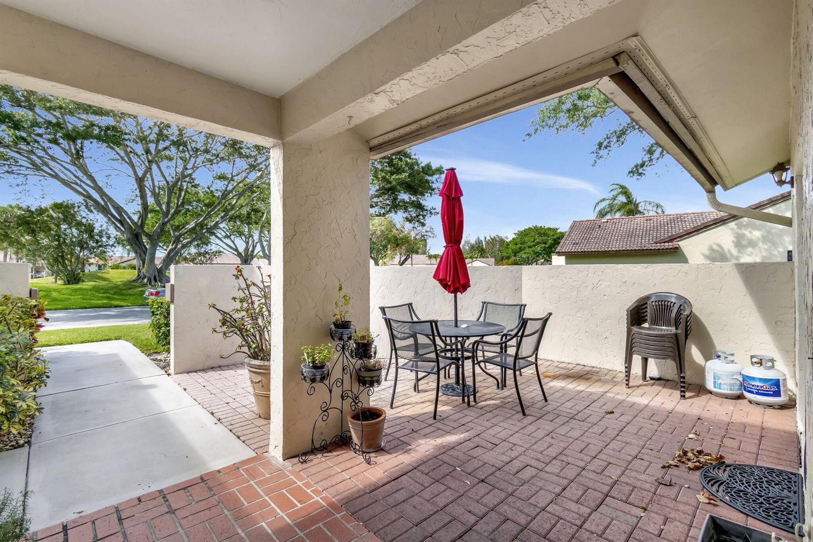 A covered brick patio features a dining set with a red umbrella and potted plants — 5531 Parkwalk Circle E, Boynton Beach FL 33472, BOYNTON BEACH, FL