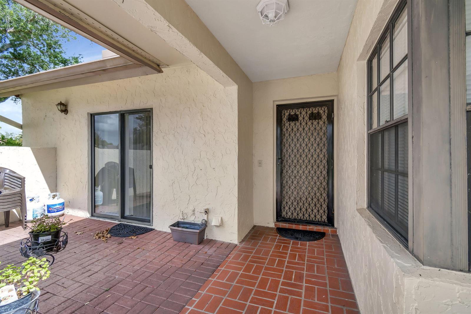 A covered patio features red brick flooring, a sliding glass door, and a security screen door — 5531 Parkwalk Circle E, Boynton Beach FL 33472, BOYNTON BEACH, FL