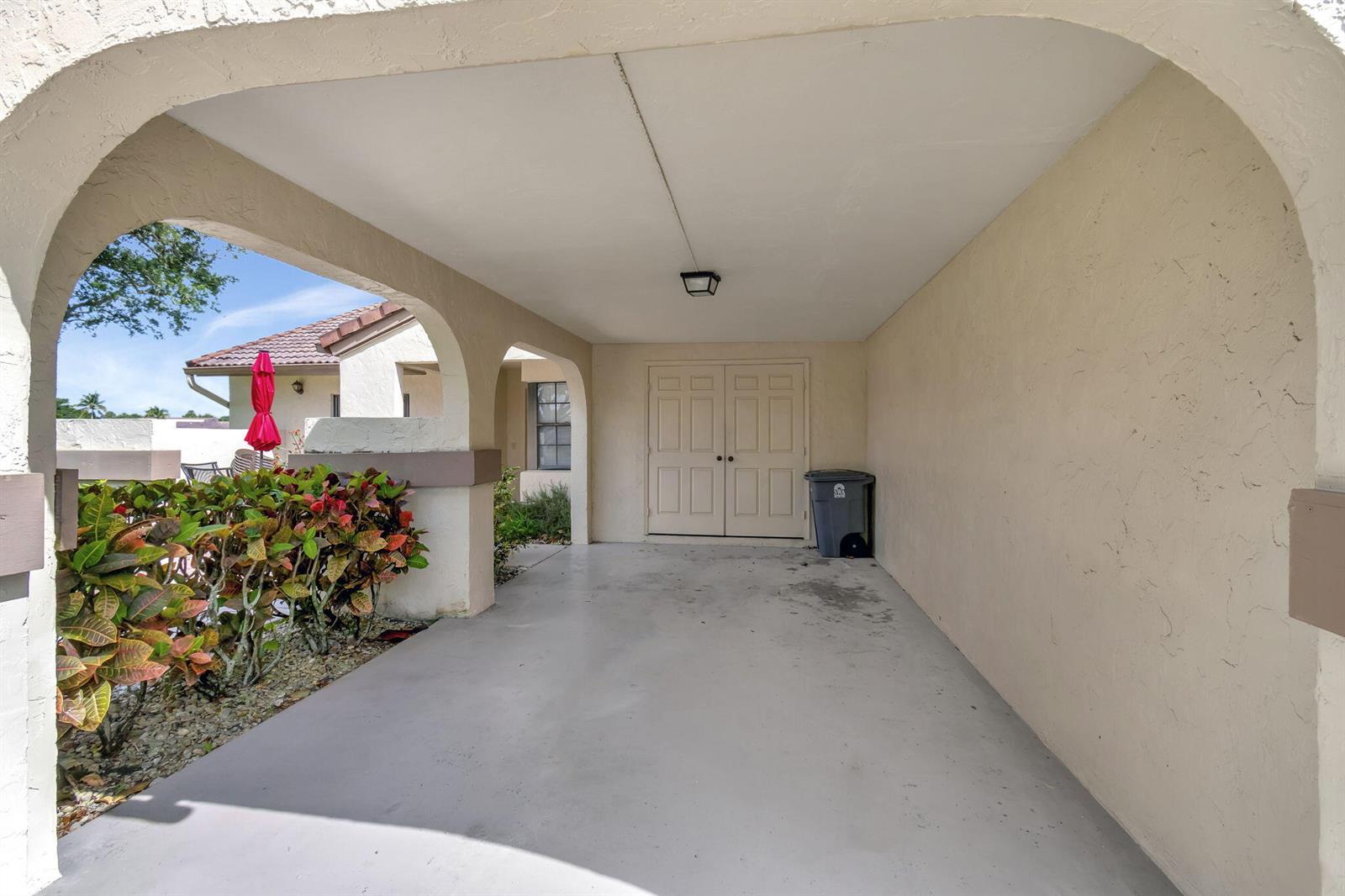 A covered carport features a concrete floor, arched openings, and double doors — 5531 Parkwalk Circle E, Boynton Beach FL 33472, BOYNTON BEACH, FL