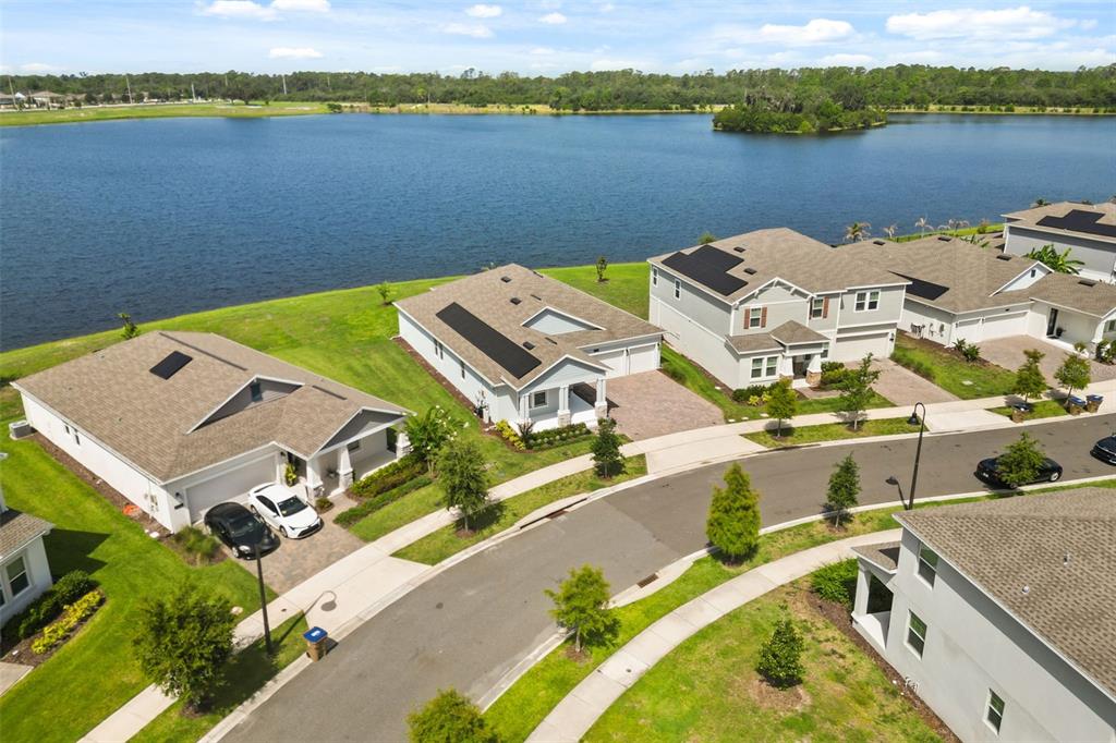 An aerial view shows several suburban houses with solar panels situated along a large lake — 3020 ELLA WAY, ST CLOUD, FL