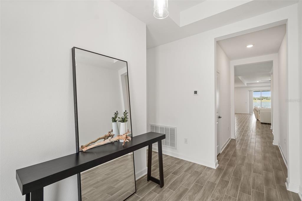 A bright entryway features a black console table, a tall mirror, and wood-look tile flooring — 3020 ELLA WAY, ST CLOUD, FL