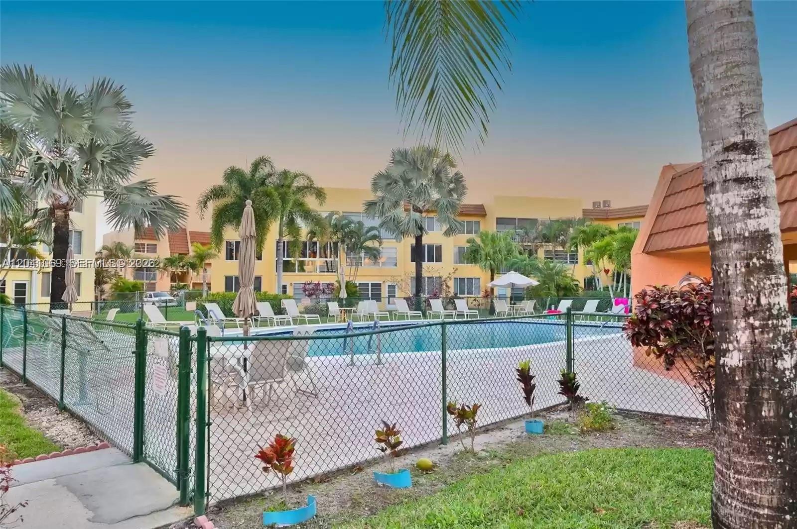 A swimming pool is enclosed by a chain-link fence in front of a multi-story apartment building — 6870 Royal Palm Blvd # 111M, Margate FL 33063, MARGATE, FL