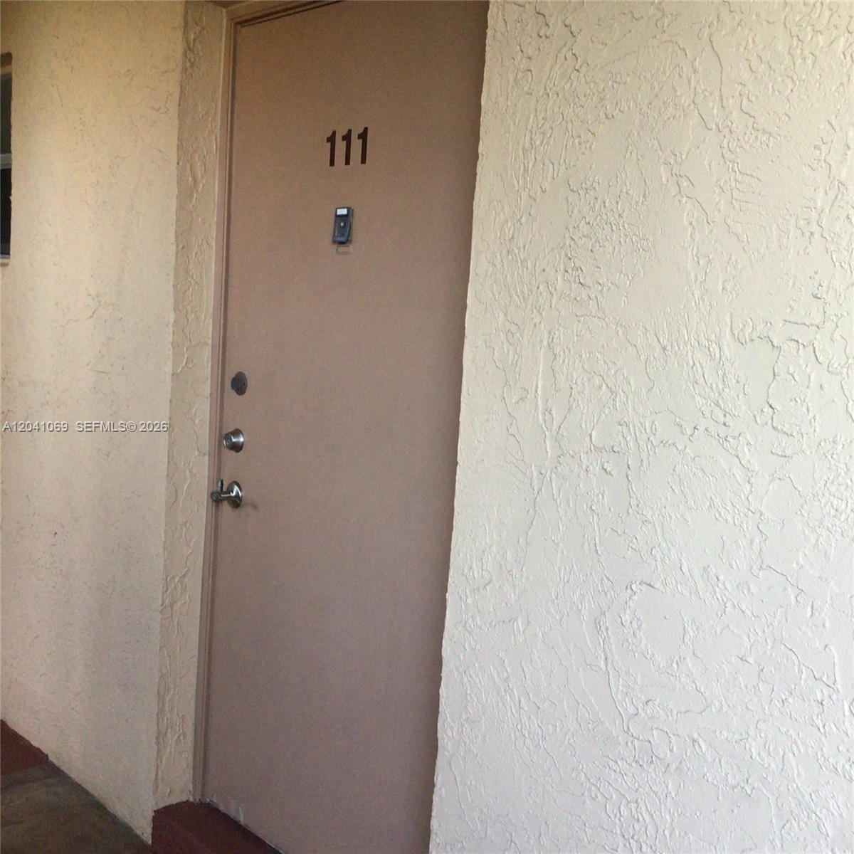 A beige door labeled 111 is set into a textured, light-colored stucco wall — 6870 Royal Palm Blvd # 111M, Margate FL 33063, MARGATE, FL