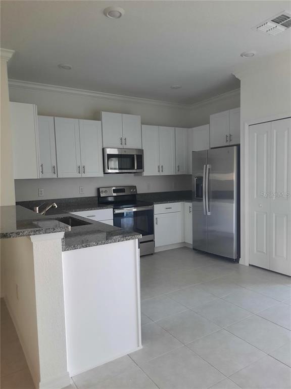 A kitchen features white cabinets, stainless steel appliances, and dark granite countertops — 36429 CAMP FIRE TERRACE, ZEPHYRHILLS, FL
