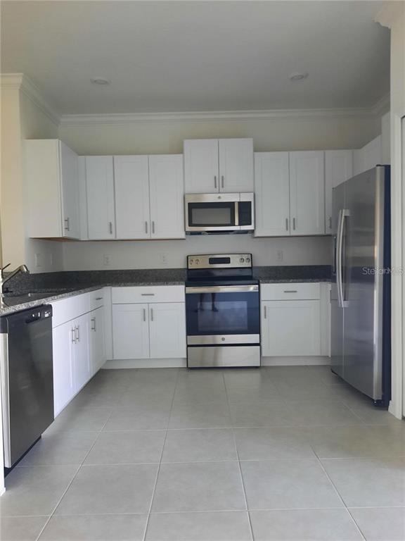A kitchen features white cabinets, stainless steel appliances, and gray granite countertops — 36429 CAMP FIRE TERRACE, ZEPHYRHILLS, FL