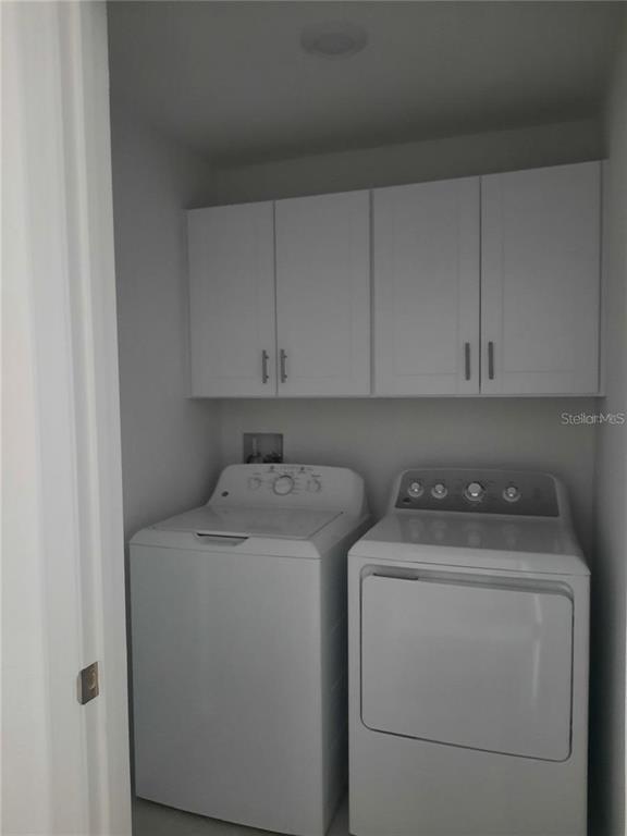 A laundry room features a white washer and dryer beneath white wall-mounted cabinets — 36429 CAMP FIRE TERRACE, ZEPHYRHILLS, FL