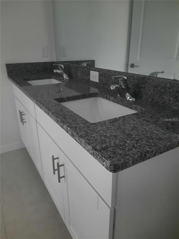A bathroom vanity features a dark granite countertop with dual sinks and white cabinets — 36429 CAMP FIRE TERRACE, ZEPHYRHILLS, FL