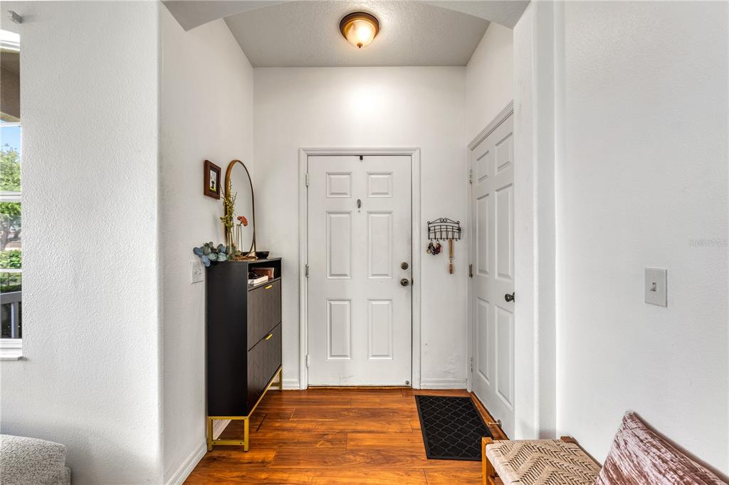 An entryway with wood flooring, a white front door, a black cabinet, and a light fixture — 14319 GNATCATCHER TERRACE, LAKEWOOD RANCH, FL