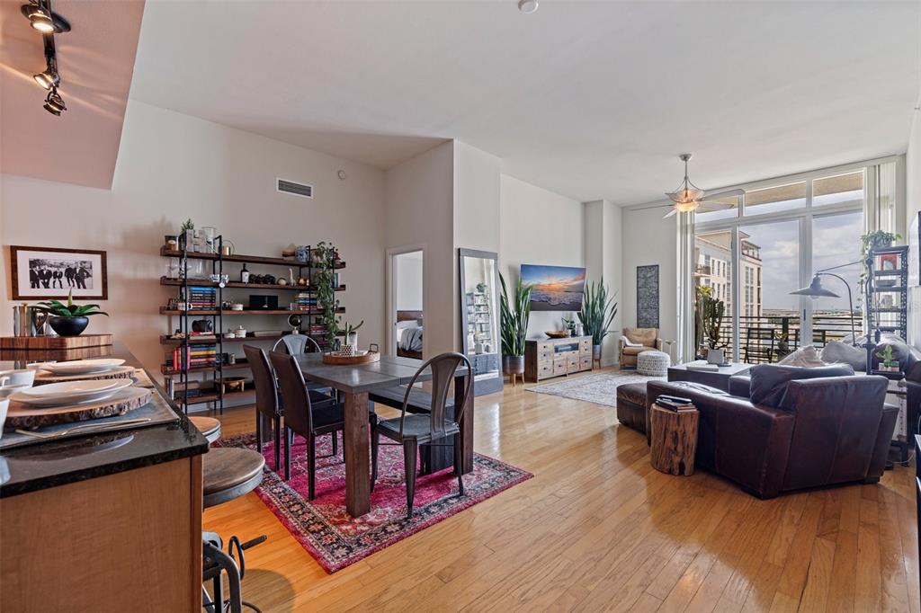 An open-concept living and dining area features hardwood floors, a leather sofa, and balcony access — 1208 E KENNEDY BOULEVARD UNIT 831, TAMPA, FL
