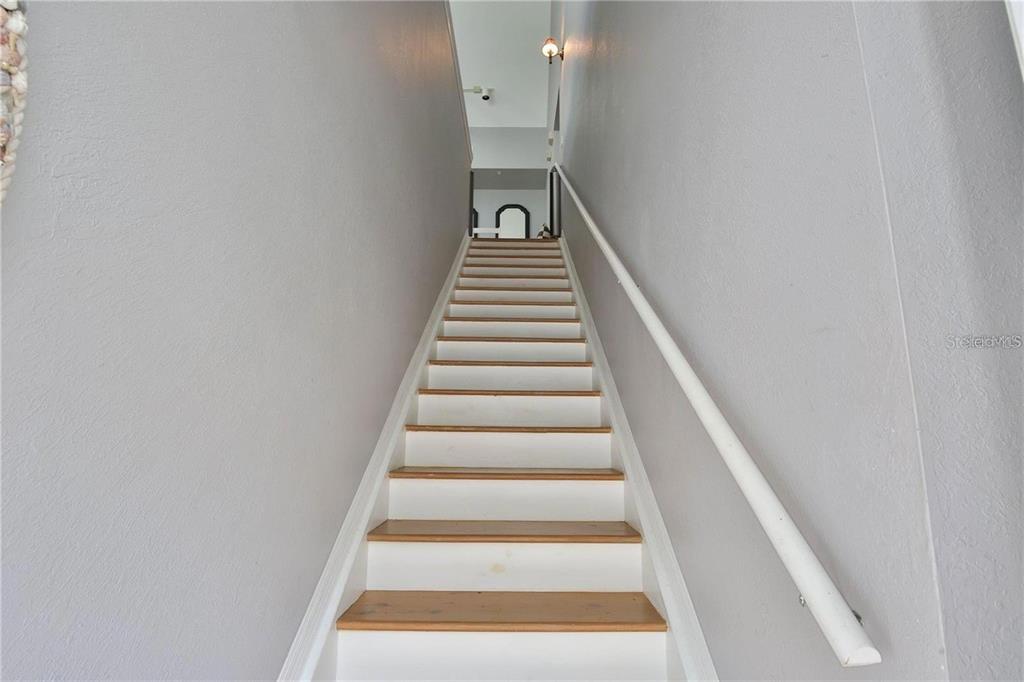 A straight wooden staircase with white risers leads upward between two gray walls — 5570 ROSEHILL ROAD UNIT 204, SARASOTA, FL