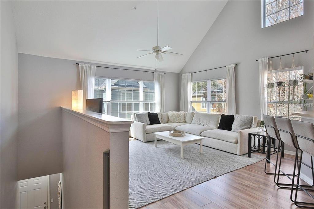 A living room with a vaulted ceiling, sectional sofa, and a half-wall overlooking a staircase — 5570 ROSEHILL ROAD UNIT 204, SARASOTA, FL