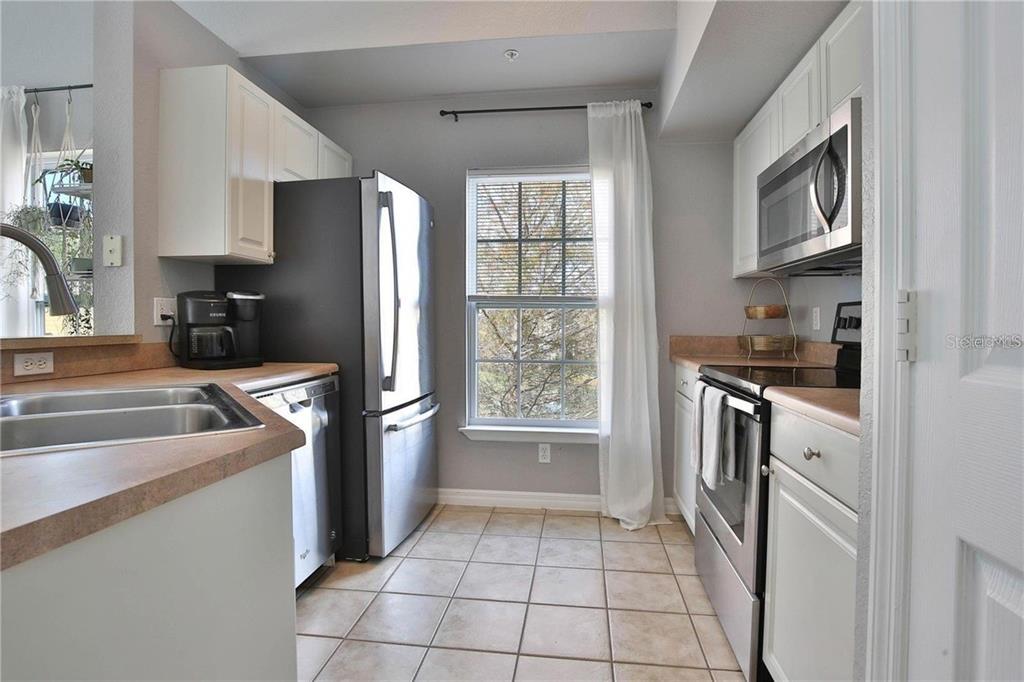 A kitchen features white cabinets, stainless steel appliances, a window with curtains, and tile flooring — 5570 ROSEHILL ROAD UNIT 204, SARASOTA, FL