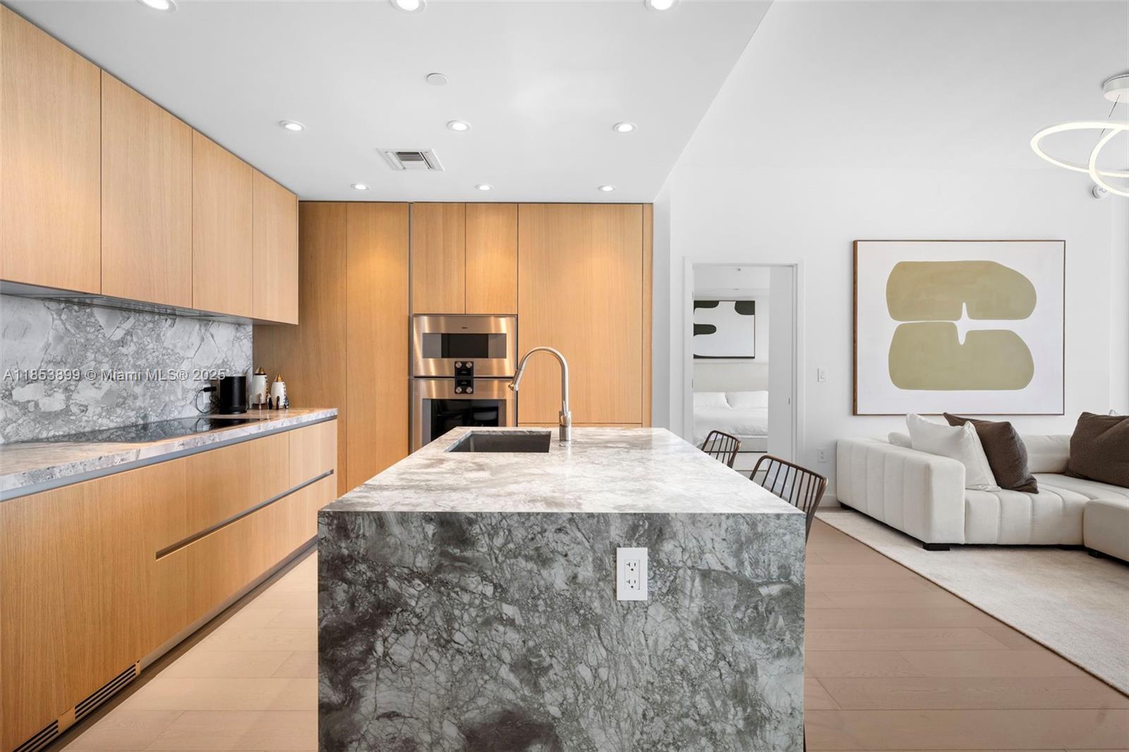 A modern kitchen features light wood cabinetry, a marble waterfall island, and an adjacent living area — 500 alton  rd # 3604, Miami Beach FL 33139, MIAMI BEACH, FL