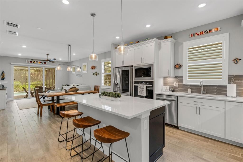 A modern kitchen features a white island with wood stools, stainless appliances, and dining area — 10374 ABACO FALLS DRIVE, ENGLEWOOD, FL