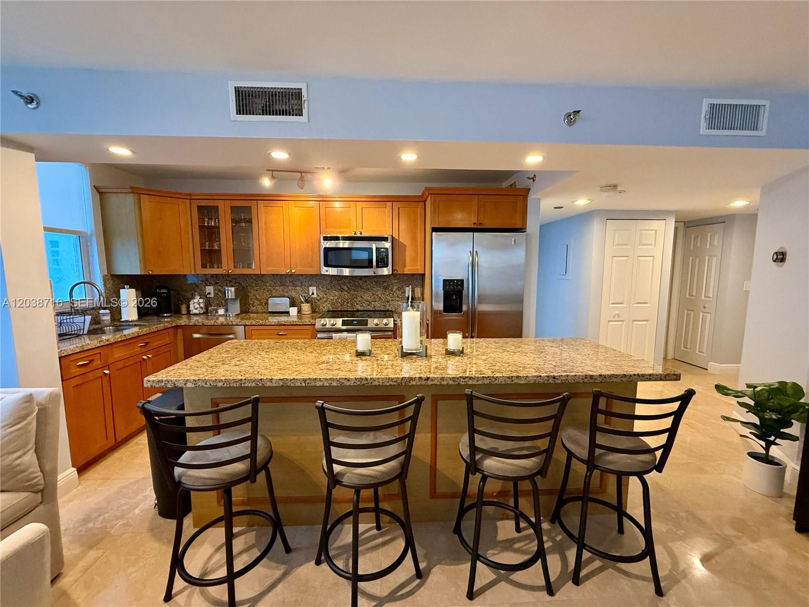 A kitchen features wooden cabinets, granite countertops, a central island with bar stools, and appliances — 770 Claughton Island Dr # 2016, Miami FL 33131, MIAMI, FL